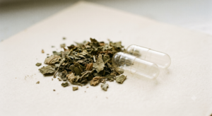 Dried crushed leaf material beside two empty clear capsule shells